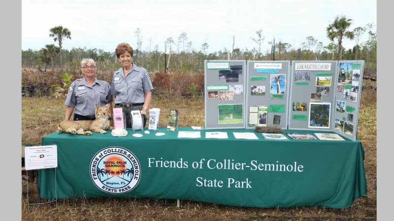 Two members from the Friends of Collier-Seminole State Park hosting display table at a park event.