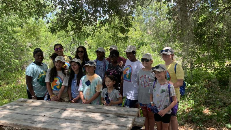 A group of Girl Scouts pose for a photo behind a picnic table.