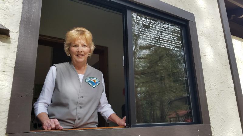 Volunteer Jerrettha French stands at the window of Ponce de Leon Springs Ranger Station ready to greet visitors with a smile. 