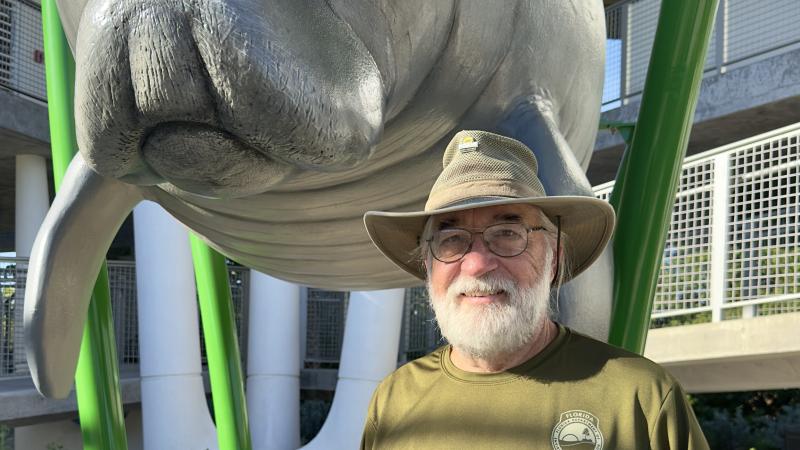 A man in a wide-brim hat standing in front of a manatee statue