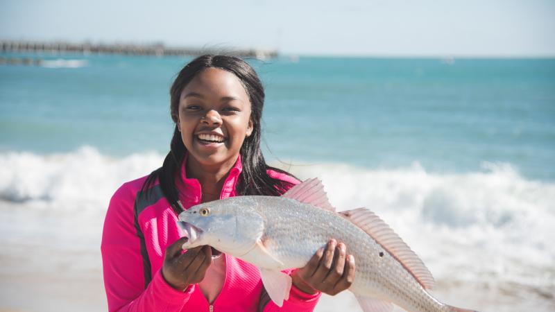 A young woman holds a red drum fish on the beach. 