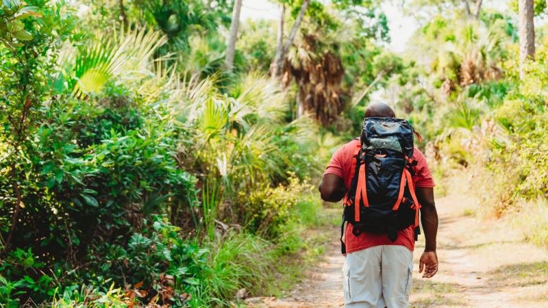 a man has his back turmed, walking on a trail with a backpack.