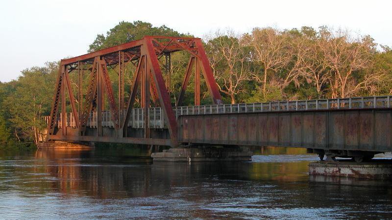 a red steel bridge span extends over a river in the morning light