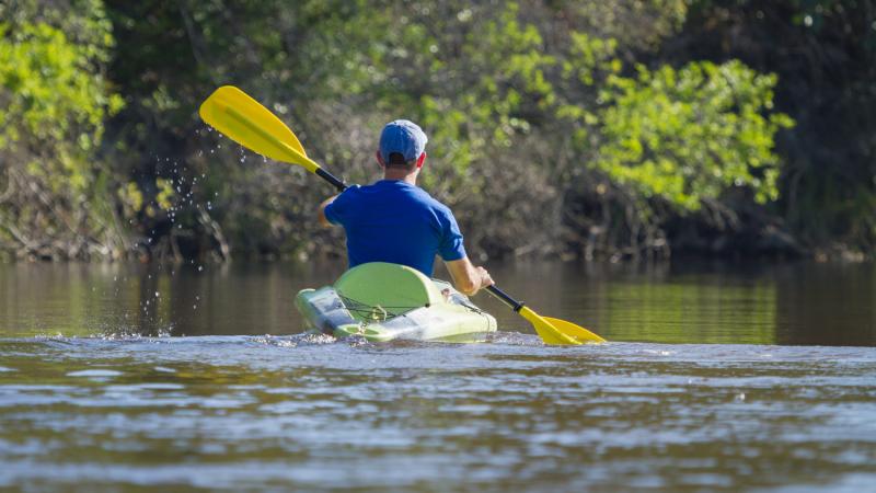 Man glides through water on green kayak. 