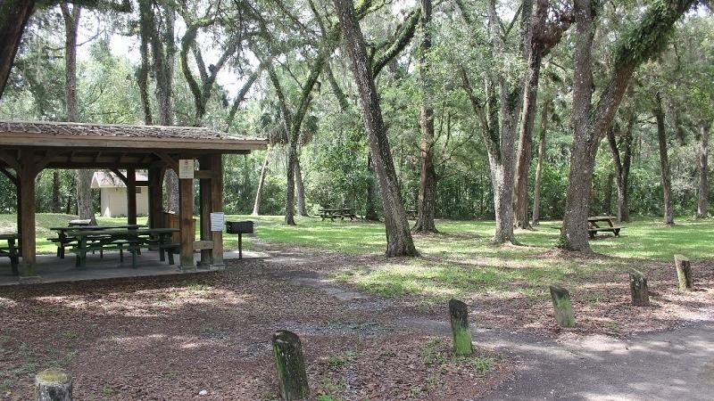 a picnic pavilion with tables sits in a lot under oak trees.