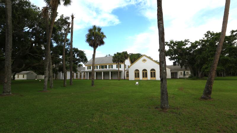 a stately house on a green lawn with palm trees