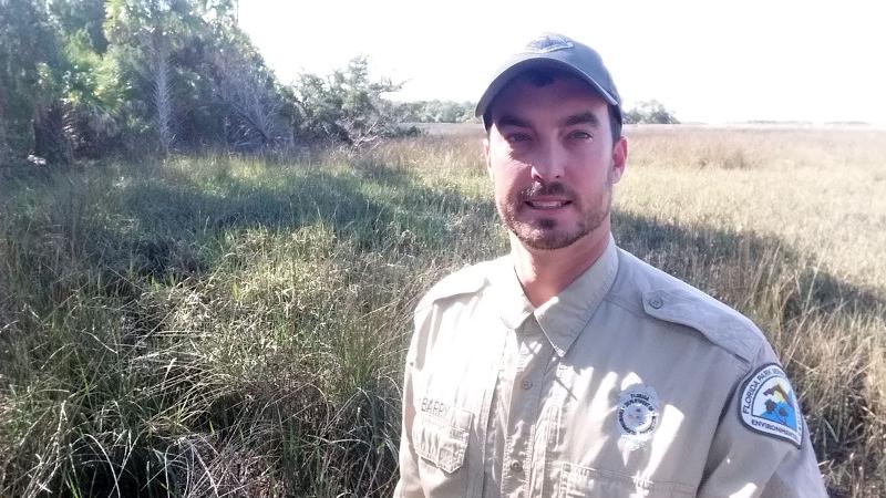 A man in uniform stands in front of a scrub habitat.