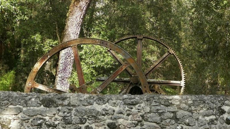Two large metal rusted wheels above a gray stone wall.
