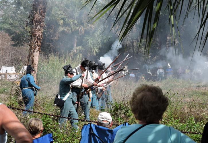 8 Reenactment actors firing historic muskets with smoke in the air and crowd watching
