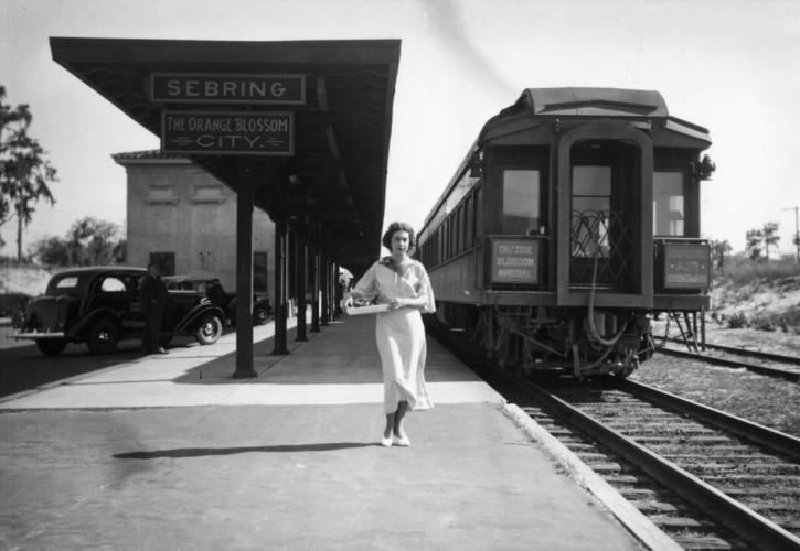 A young woman stands near the Orange Blossom Special train at railroad depot - Sebring, Florida. 1930