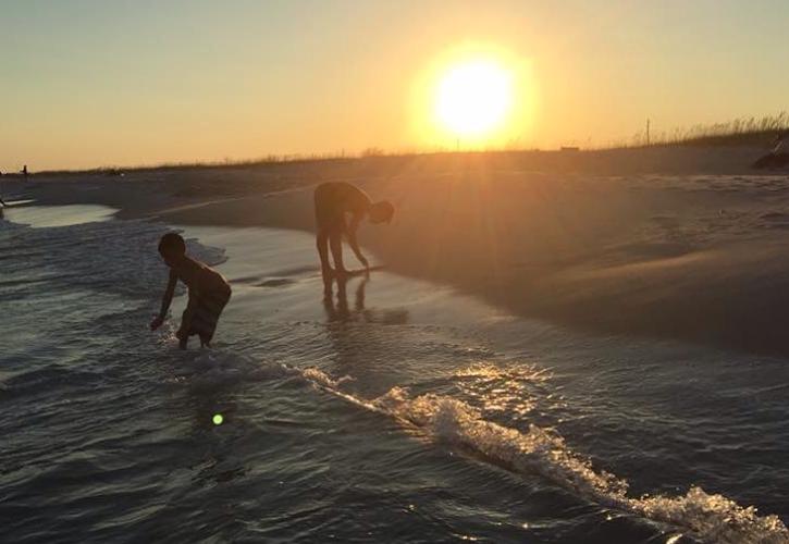 Two children play in the waves with setting sun in the background. 