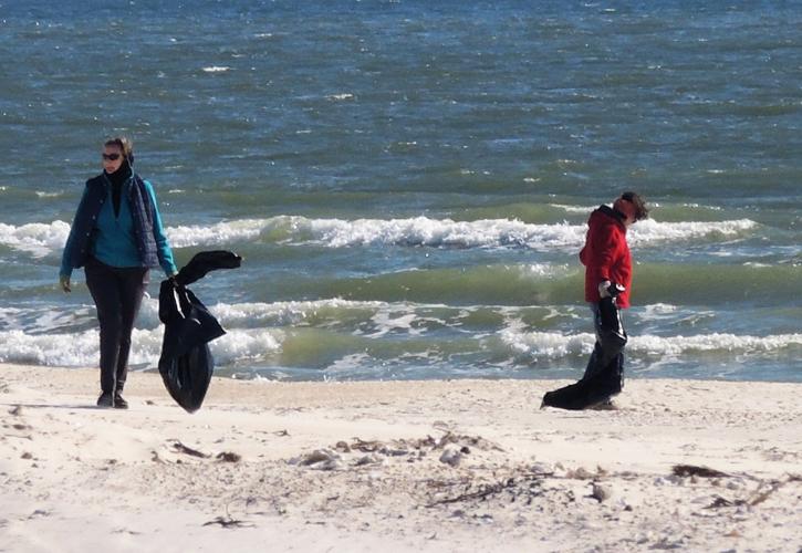 Volunteers comb the beach with trash bag in hand collecting debris left after Hurricane Michael. 