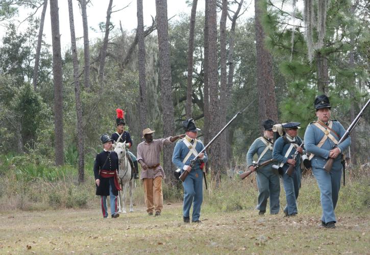 A group of reenactors walking through the woods.