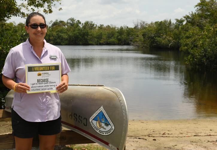 Woman standing near a canoe and water on the beach holding a sign