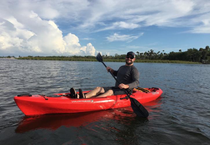 a man paddles a red kayak on a river.