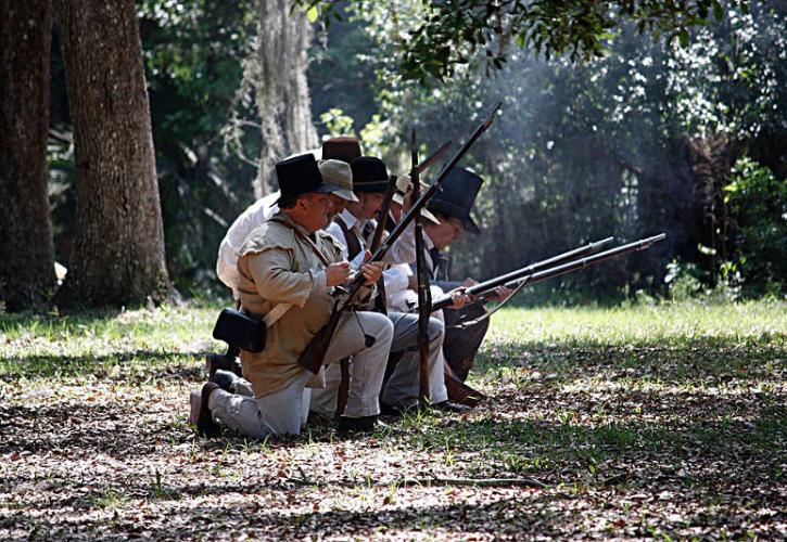 a line of men loads muskets while kneeling.