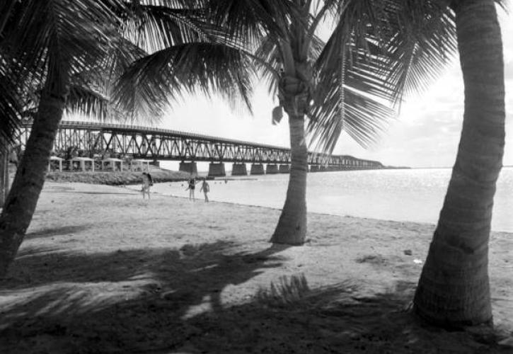 Three people walk the shoreline near the bridge in 1954.