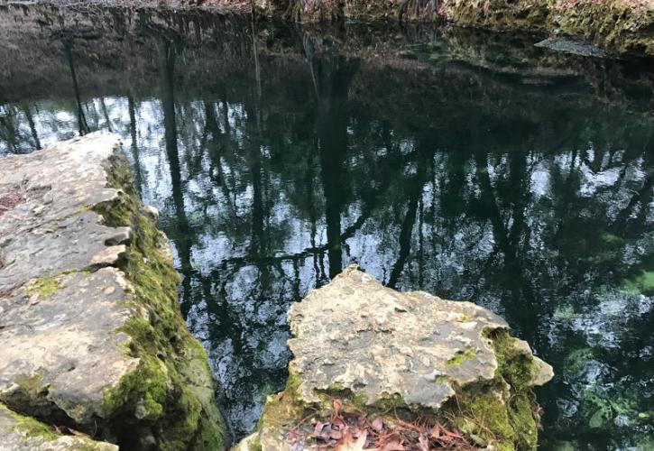 Two limestone rock outcroppings extend over dark water on the banks of a spring