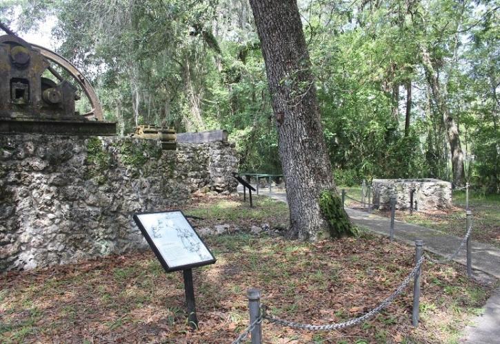 a path lined with trees and signs runs alongside a stone structure