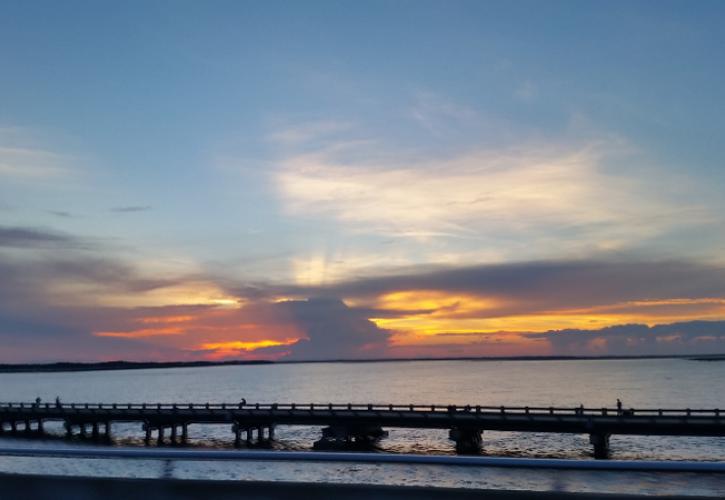 the sun rises over a concrete bridge over water