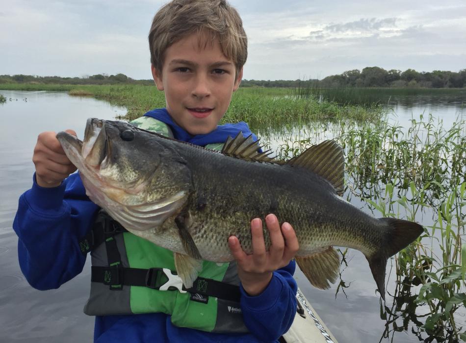 A young man shows off the large mouth bass he caught on Myakka Lake.