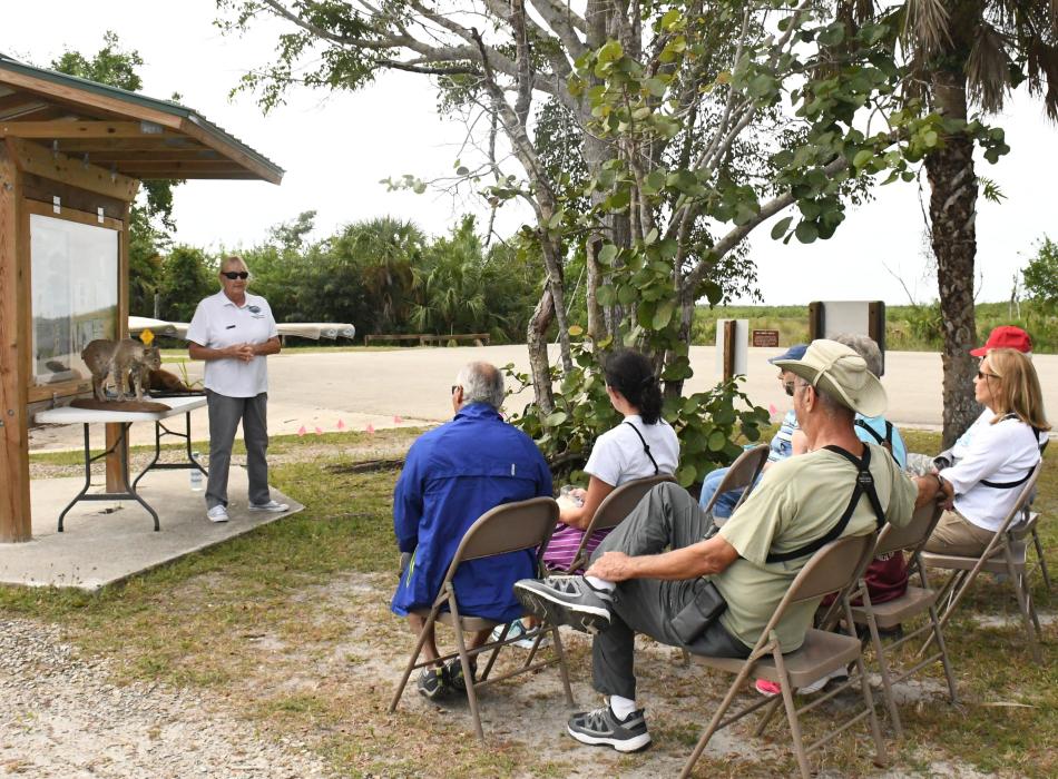 Woman standing during a presentation about mangroves to a group of adults sitting in chairs at the salt marsh.