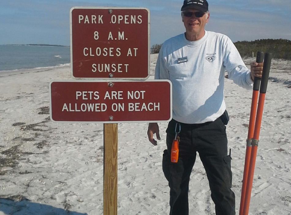 Steve Lilly standing next to a sign on the beach.