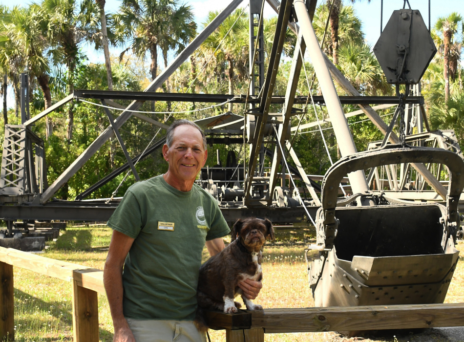 Man with dog standing at dredge machine with trees