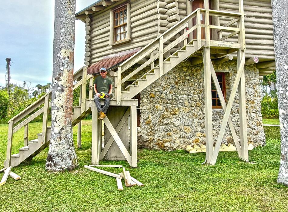 Man sitting on wooden steps of a log building green grass blue sky