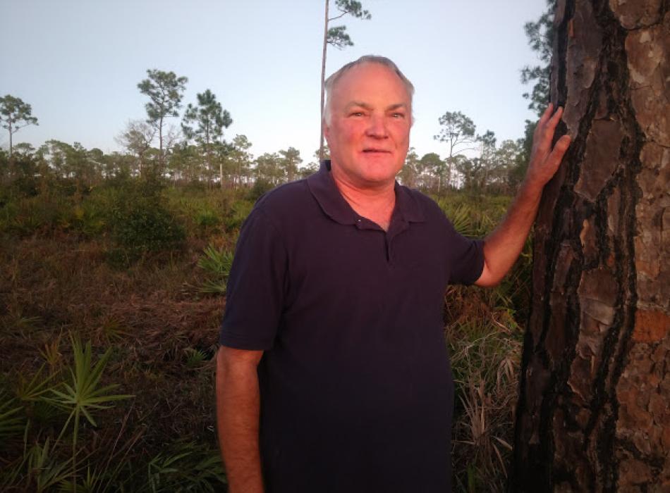 Chris Bertram, standing by a tree in during sunset, smiling at the camera.