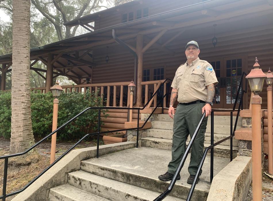 Park Ranger Clayton Iron Wolf stand on the steps leading up to the Lodge at Camp Helen State Park. 