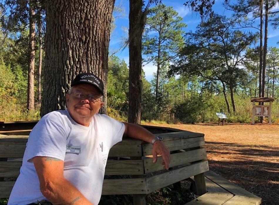 a man in a volunteer shirt and hat lounges on a bench in a park