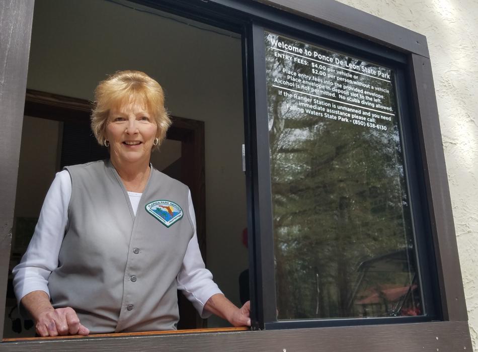 Volunteer Jerrettha French stands at the window of Ponce de Leon Springs Ranger Station ready to greet visitors with a smile. 