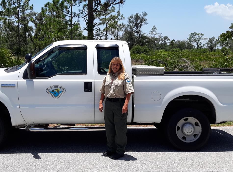 Lyndel Mclellen standing in front of a truck, wearing her ranger uniform and smiling at the camera.