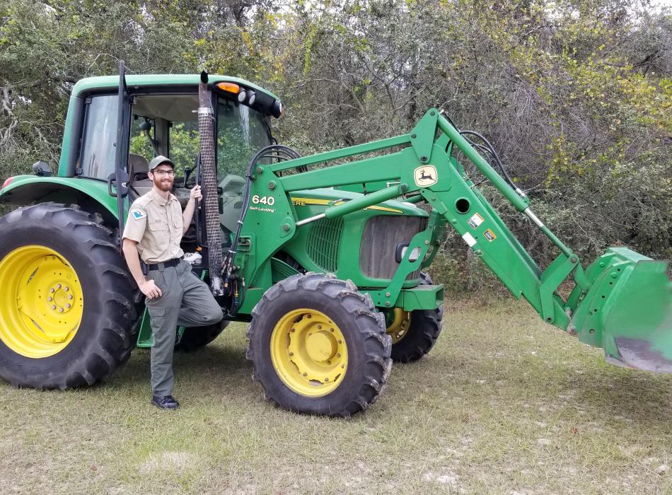 Park Ranger Kyle Blair standing next to a tractor and smiling at the camera