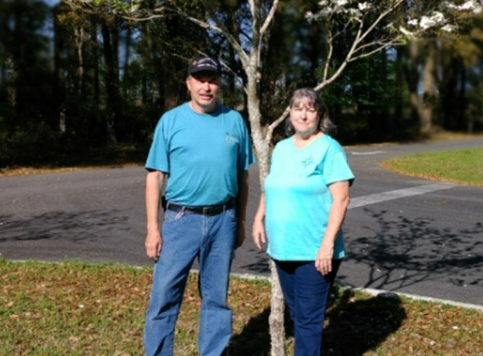 a man and woman in blue shirts stand next to a tree.