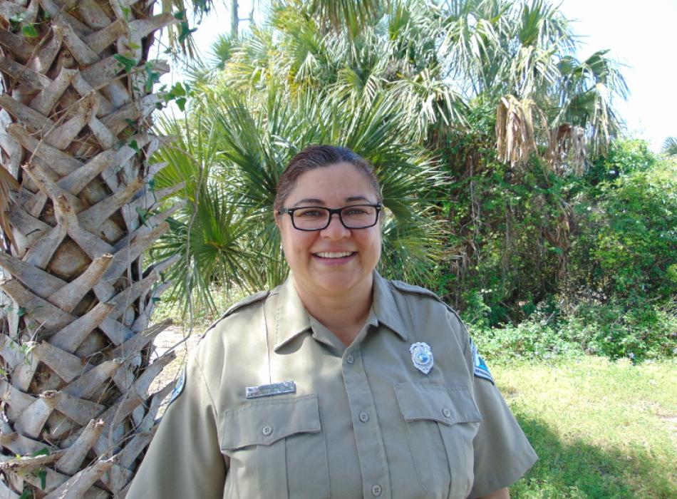 a woman in park service uniform stands in front of a palm tree