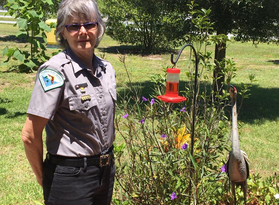 Volunteer Peggy Thibodeaux smiling for the camera next to a hummingbird feeder