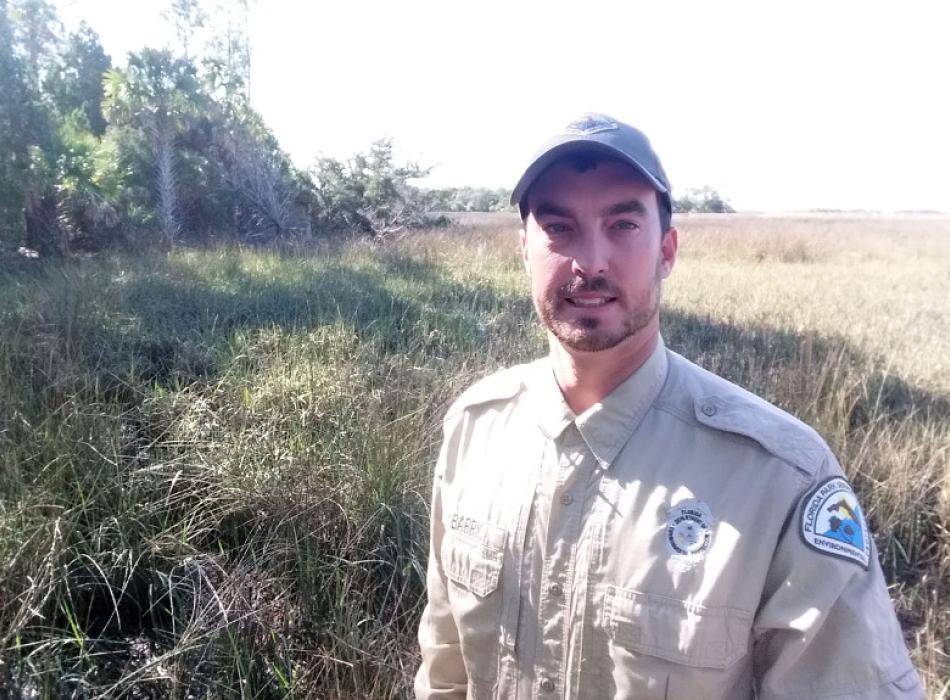 A man in uniform stands in front of a scrub habitat.